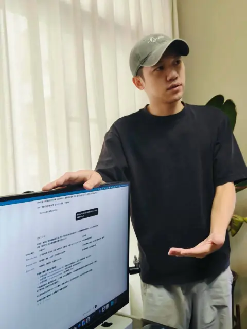 小刁站在螢幕旁邊,一手比著講解