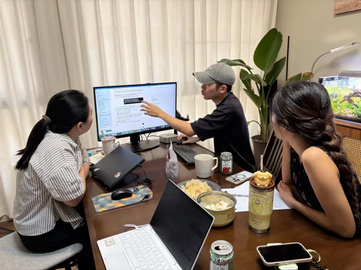 小刁指著螢幕講解，兩位夥伴坐在桌邊一起看
